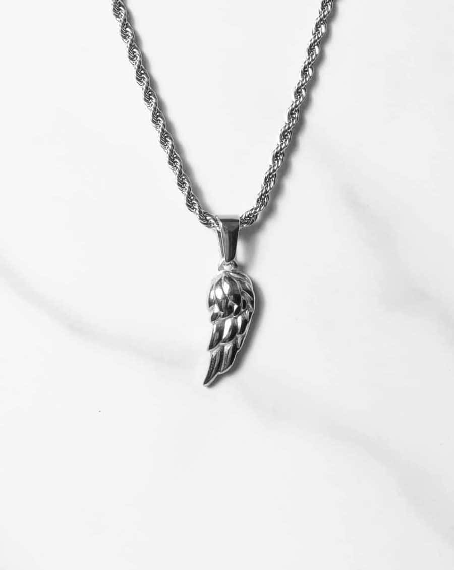 Ett silverhalsband med en tvinnad repkedja har ett Angel Wing Silver-hänge, elegant placerat på en vit marmoryta.
