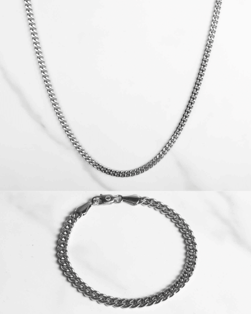 Ett silverfärgat Pansarlänk set silver 5mm halsband och matchande armband visas på en vit yta och framhäver deras eleganta, polerade curb-link design.