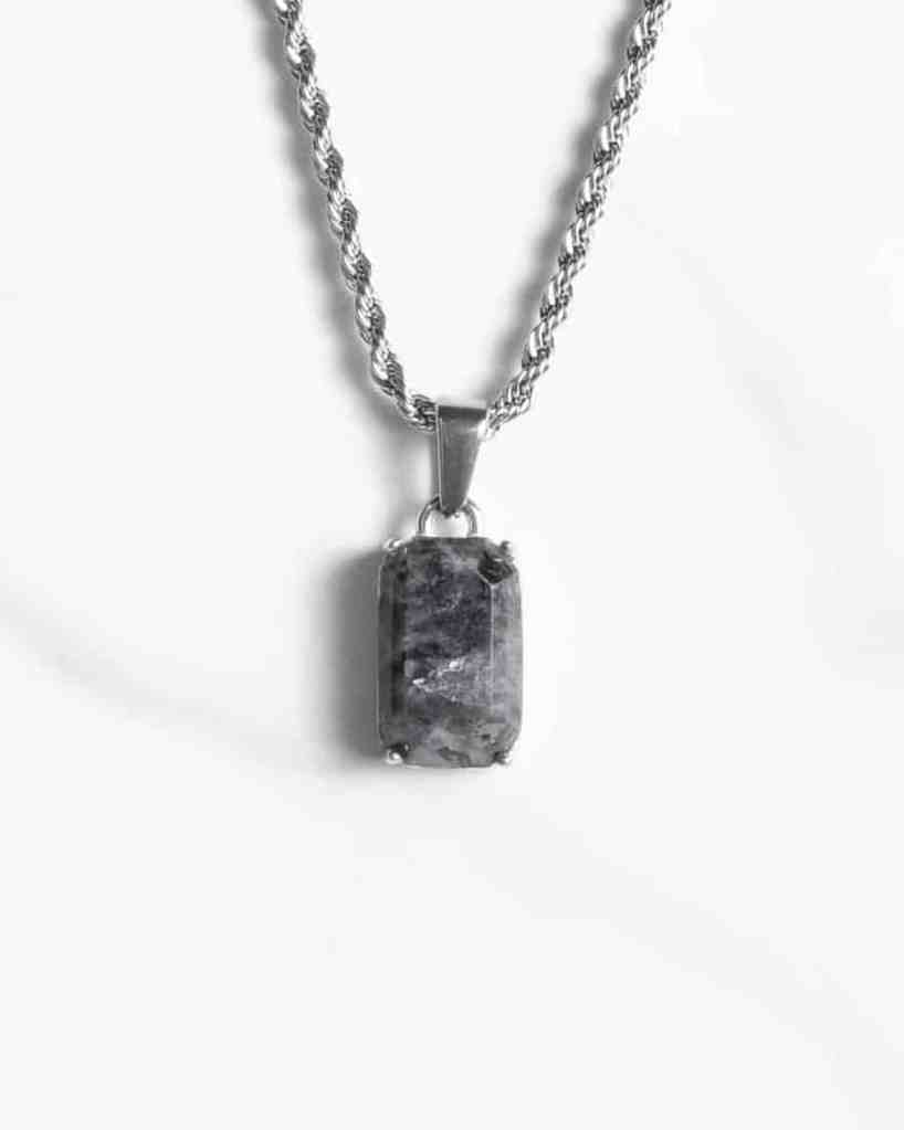 Ett silverhalsband med ett rektangulärt hänge i form av en marmorerad sten av svart onyx visas mot en vit bakgrund.